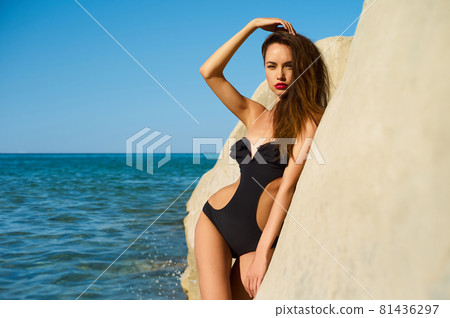 Beautiful elegant lady poses on the beach in black swimming suit Beautiful elegant lady poses on the beach in black swimming suit 81436297