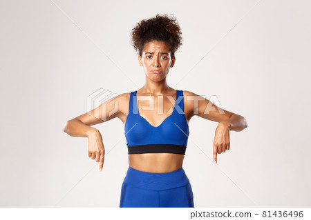 Concept of workout and fitness. Sad and gloomy african-american girl athelte, wearing blue sportswear, pointing fingers down and sobbing, white background 81436496