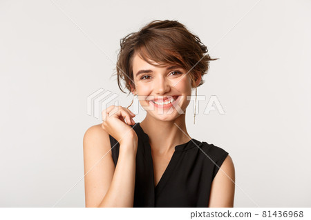 Close-up of elegant businesswoman smiling at camera satisfied, standing over white background Close-up of elegant businesswoman smiling at camera satisfied, standing over white background 81436968