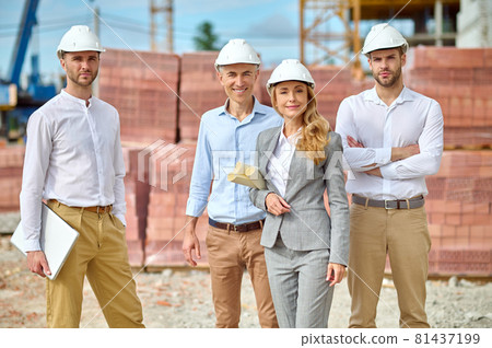 Confident lady supervisor and workers in hardhats standing outside Confident lady supervisor and workers in hardhats standing outside 81437199