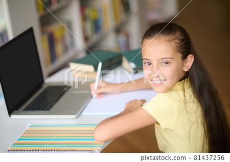 Pleased schoolgirl taking notes in her notebook Pleased schoolgirl taking notes in her notebook 81437256