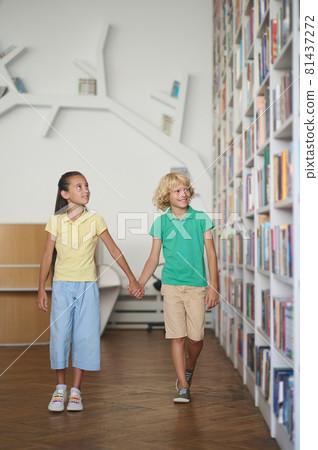Two children impressed by a variety of books on the shelves Two children impressed by a variety of books on the shelves 81437272