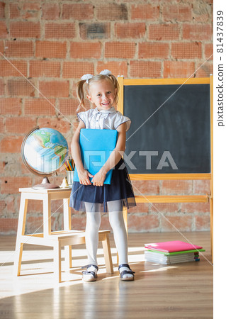 Adorable schoolgirl smiling in front of blackboard with book in her hands Adorable schoolgirl smiling in front of blackboard with book in her hands 81437839