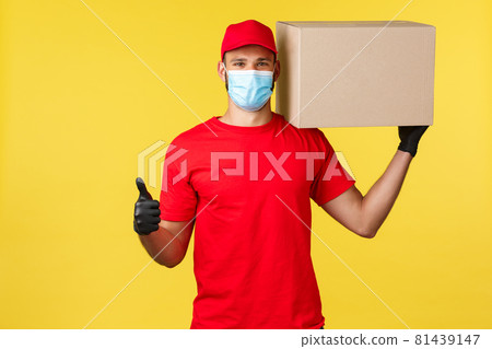 Express delivery during pandemic, covid-19, safe shipping, online shopping concept. Strong young courier in red uniform of company, hold box on shoulder and thumb-up, guarantee safety of parcel Express delivery during pandemic, covid-19, safe shipping, online shopping concept. Strong young courier in red uniform of company, hold box on shoulder and thumb-up, guarantee safety of parcel 81439147