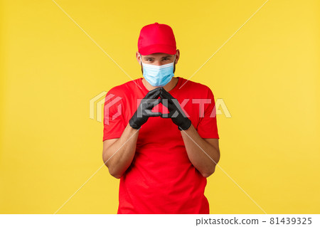 Express delivery during pandemic, covid-19, safe shipping, online shopping concept. Devious and creative young courier in red uniform and medical mask, have plan, scheming over yellow background Express delivery during pandemic, covid-19, safe shipping, online shopping concept. Devious and creative young courier in red uniform and medical mask, have plan, scheming over yellow background 81439325