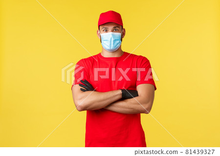 Express delivery during pandemic, covid-19, safe shipping, online shopping concept. Surprised male courier in red uniform cap and t-shirt, cross arms chest, medical mask, stand yellow background Express delivery during pandemic, covid-19, safe shipping, online shopping concept. Surprised male courier in red uniform cap and t-shirt, cross arms chest, medical mask, stand yellow background 81439327