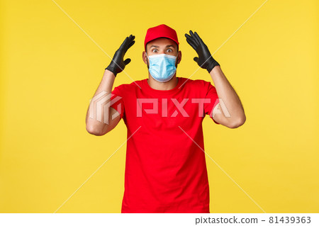 Express delivery during pandemic, covid-19, safe shipping, online shopping concept. Excited and startled young courier found out mindblowing info, show boom, wear medical mask 81439363