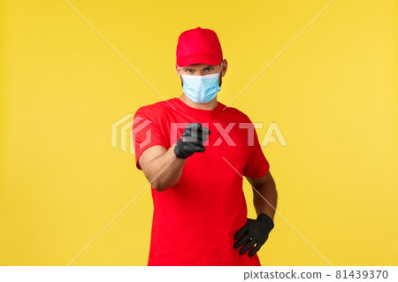 Express delivery during pandemic, covid-19, safe shipping, online shopping concept. Confident serious courier in medical mask and gloves, pointing finger at camera, yellow background Express delivery during pandemic, covid-19, safe shipping, online shopping concept. Confident serious courier in medical mask and gloves, pointing finger at camera, yellow background 81439370