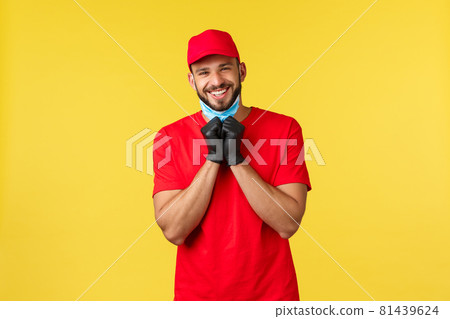 Express delivery during pandemic, covid-19, safe shipping, online shopping concept. Friendly charismatic courier in red uniform, gloves, take-off medical mask to smile sincere, yellow background 81439624