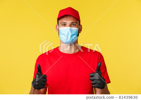 Covid-19, delivery orders, shopping, contactless payment and social distancing concept. Cheerful and supportive courier in red uniform cap and t-shirt, medical mask gloves, show thumbs-up 81439630