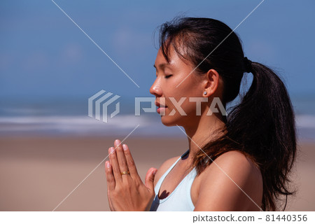 people, fitness, sport and healthy lifestyle concept - close up portrait of young asian woman making meditation on tropical beach with blue sky background people, fitness, sport and healthy lifestyle concept - close up portrait of young asian woman making meditation on tropical beach with blue sky background 81440356