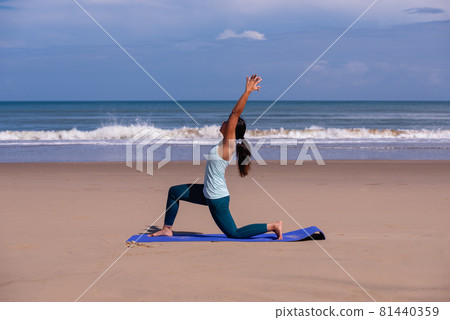 people, fitness, sport and healthy lifestyle concept - young asian woman making warrior yoga poses on tropical beach with blue sky background 81440359