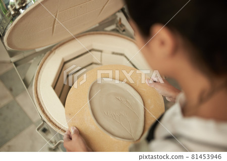 Woman putting clay plate into kiln 81453946