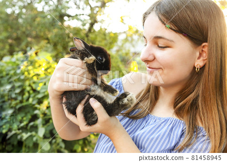 Teen girl in blue striped dress holding fluffy adorable bunny with hands Teen girl in blue striped dress holding fluffy adorable bunny with hands 81458945