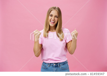 Yes I did it. Portrait of happy delighted successful young female student receiving award triumphing being excited and joyful raising clenched fists in cheer, gazing confident at camera over pink wall 81459347