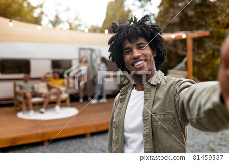 Funky black guy taking selfie near RV, resting with diverse friends outdoors, enjoying autumn camping trip, copy space 81459587