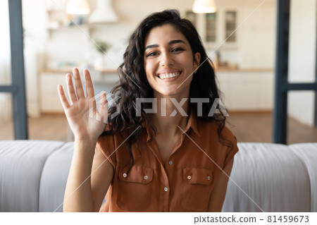 Cheerful young woman calling her friend on webcam, talking to family remotely from home, waving at camera Cheerful young woman calling her friend on webcam, talking to family remotely from home, waving at camera 81459673