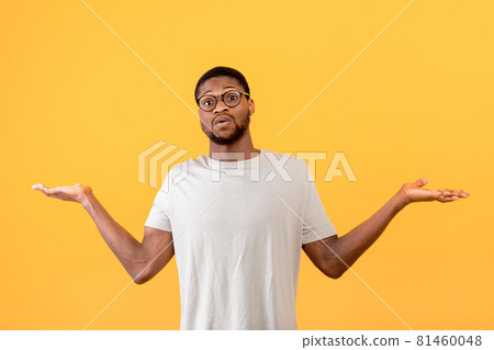 Confused black guy raising hands up and looking at camera, standing over yellow studio background Confused black guy raising hands up and looking at camera, standing over yellow studio background 81460048