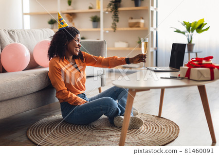 African Woman Stretching Glass To Laptop Celebrating Birthday Online Indoor African Woman Stretching Glass To Laptop Celebrating Birthday Online Indoor 81460091