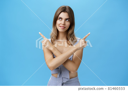 Creative intrigued attractive woman in matching clothes biting lip from desire and interest looking at upper left corner as if having plan crossing hands and pointing in different directions Creative intrigued attractive woman in matching clothes biting lip from desire and interest looking at upper left corner as if having plan crossing hands and pointing in different directions 81460333