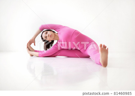 Young slender fit woman in pink long bodysuit performing yoga pose, isolated over white studio background 81460985