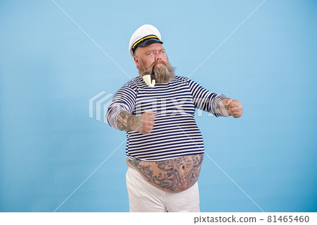 Obese captain with vintage smoking pipe holds invisible helm on light blue background Obese captain with vintage smoking pipe holds invisible helm on light blue background 81465460