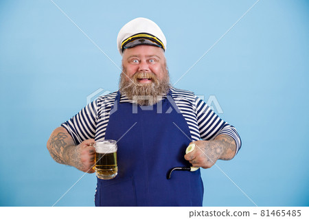 Funny plump person in sailor costume holds smoking pipe and beer on light blue background 81465485