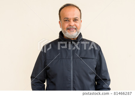 Portrait of happy bearded Indian man smiling against plain wall 81466287