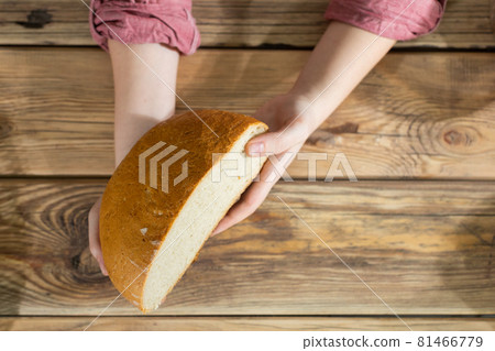 Women's hands hold half of a round wheat bread over a wooden counter. Women's hands hold half of a round wheat bread over a wooden counter. 81466779