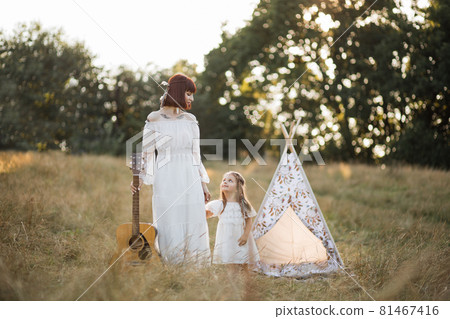 Hippie boho family, mother and little girl, walking with guitar in the summer field at sunset Hippie boho family, mother and little girl, walking with guitar in the summer field at sunset 81467416