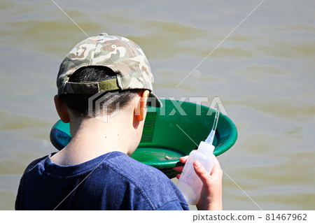 A boy looks into a gold pan with a suction bottle in hand A boy looks into a gold pan with a suction bottle in hand 81467962