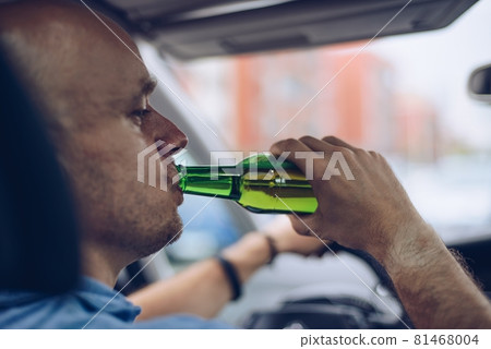 Man drives a car with a bottle of beer behind. 81468004