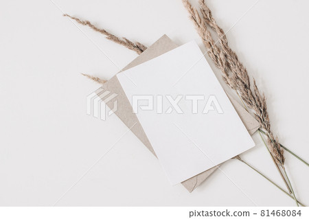 Autumn wedding, birthday stationery composition. Blank greeting card, invitation mockup, craft envelope. Dry grass, festuca plant isolated on white table background. Fall flat lay, top view. Copyspace 81468084