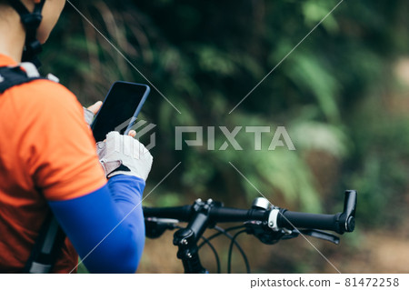 Woman cyclist use smartphone when riding mountain bike on forest trail Woman cyclist use smartphone when riding mountain bike on forest trail 81472258