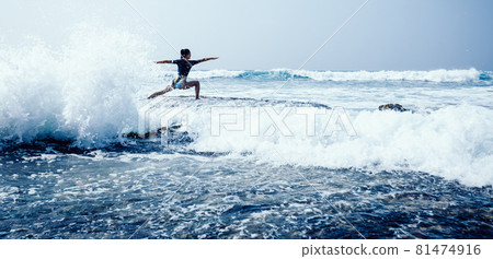 Woman practice yoga at seaside cliff edge facing the coming strong sea waves 81474916