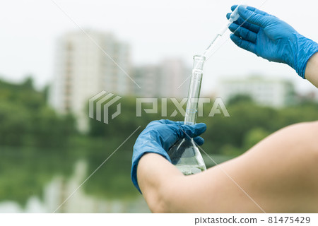 Sampling from open water. A scientist or biologist takes a sample of water from a city reservoir. A sample of water in a round chemical flask with a pipette 81475429