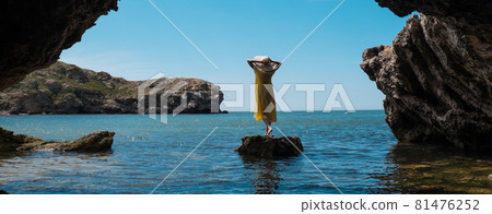 A woman in a white dress and a black hat standing on the rocks by the sea A woman in a white dress and a black hat standing on the rocks by the sea 81476252