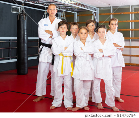 Portrait of group of children in white kimono with trainer in gym 81476784