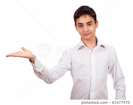 Smiling guy in white clothes on a white background looks at the camera and shows an empty palm. Cheerful young man in white shirt shows on blank space 81477470