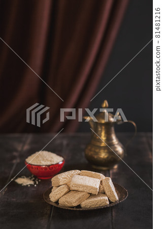 Pieces of tahini halva, sesame seeds in a bowl, an vintage jug.. Still life in the oriental style on an old brown wooden background, copy space Pieces of tahini halva, sesame seeds in a bowl, an vintage jug.. Still life in the oriental style on an old brown wooden background, copy space 81481216