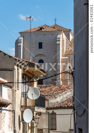 View of small town with church and picturesque houses with plastered facade and ceramic tile roofs on a sunny day 81483061