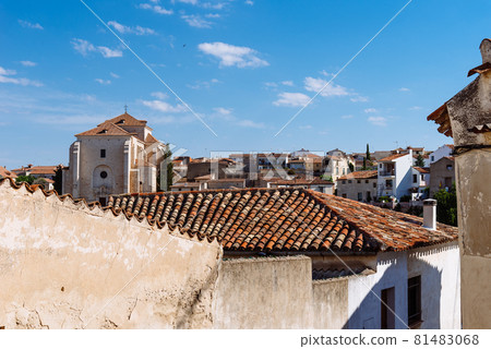 View of small town with church and picturesque houses with plastered facade and ceramic tile roofs on a sunny day 81483068