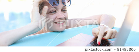 Young smiling woman is working on laptop while in pool Young smiling woman is working on laptop while in pool 81483806