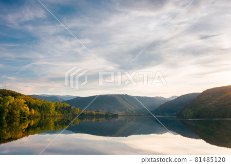 beautiful autumn landscape by the lake at sunset. trees in colorful foliage and forested apuseni mountains reflecting in the water surface. clouds on the sky in evening light 81485120