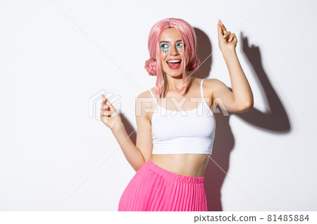Image of attractive party girl with pink wig and bright makeup, having fun and celebrating holiday, dancing happy over white background 81485884