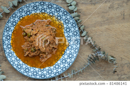 Panaeng curry with pork or Dried red pork coconut curry in a ceramic plate on wooden background. Panaeng curry with pork or Dried red pork coconut curry in a ceramic plate on wooden background. 81486141