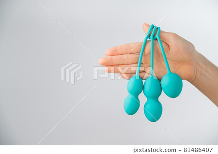 A faceless woman demonstrates a set of mint-colored vaginal balls. Girl holding a kegel trainer for training pelvic floor muscles on a white background. A faceless woman demonstrates a set of mint-colored vaginal balls. Girl holding a kegel trainer for training pelvic floor muscles on a white background. 81486407