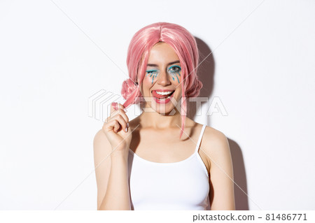 Portrait of sassy attractive girl in pink wig, wearing outfit for halloween party, smiling and winking at camera, standing over white background Portrait of sassy attractive girl in pink wig, wearing outfit for halloween party, smiling and winking at camera, standing over white background 81486771