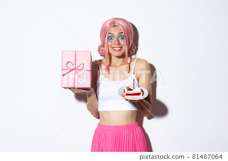 Portrait of excited birthday girl celebrating her holiday, holding b-day gift and cake, smiling happy, standing over white background 81487064