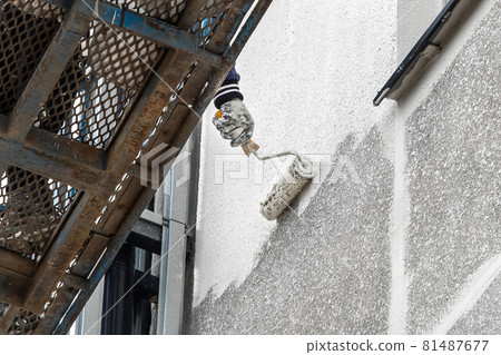 A industrial worker on a lifting platform paints the facade of a new modern urban building under construction at a construction site 81487677